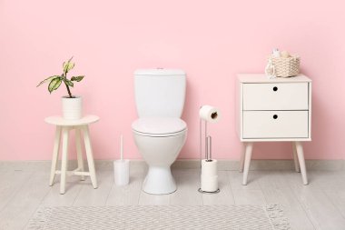 Tuvaletin içinde klozet, komodin ve pembe duvarlı kahve masası var.