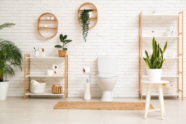 Tuvalet klozeti ve beyaz tuğla duvarın yanında raf üniteleri olan tuvaletin içinde.