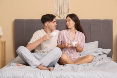 Genç çift yatakta kahve içiyor.