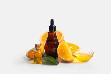 Şişeler ve cam kase portakal yağı ve gri arka planda taze meyveler.