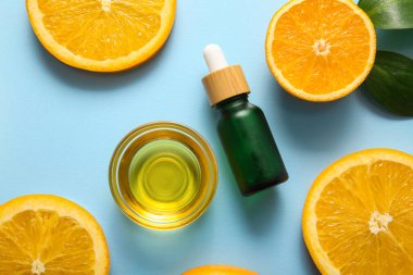 Şişe ve cam kase portakal yağı ve mavi arka planda taze meyve dilimleri