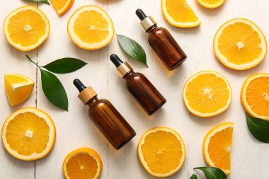 Portakal yağı şişeleri ve beyaz ahşap arka planda taze meyveler.