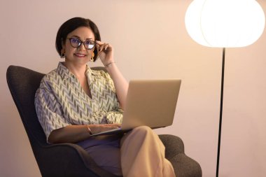 Akşam evde dizüstü bilgisayar kullanan olgun bir kadın.