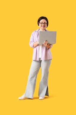 Sarı arka planda dizüstü bilgisayar kullanan olgun bir kadın