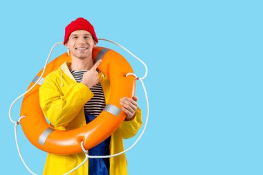 Kurtarma yüzüğüyle mavi arka plandaki bir şeyi işaret eden erkek denizci.