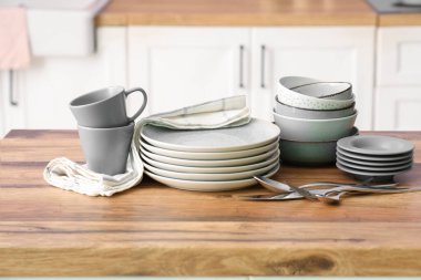 Temiz tabaklar, çatal bıçak takımı, kâseler ve bardaklar mutfaktaki ahşap tezgahta, yakın plan.