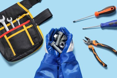 Mavi arka planda sürgüleri, fındıkları ve aletleri tutan tamircinin elleri