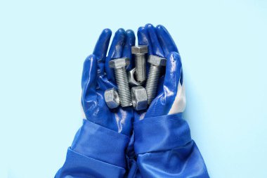 Tamircinin elleri mavi arka planda cıvata ve fındık tutuyor