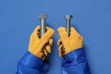 Tamircinin elleri mavi arka planda cıvataları tutuyor.