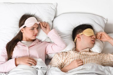 Horlayan kocasıyla yatakta yatan genç, rahatsız bir kadın.