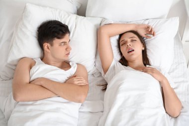 Evde horlayan karısıyla yatakta yatan sinirli genç bir adam.