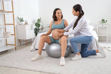 Hamile bir kadının yatak odasında spor eğitimi aldığı genç Asyalı doğum koçu.