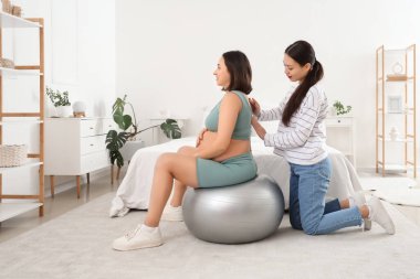 Hamile bir kadının yatak odasında spor eğitimi aldığı genç Asyalı doğum koçu.