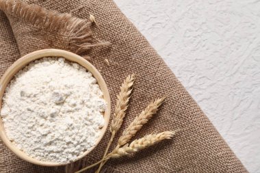 Açık arkaplanda bir kase buğday unu, dikenler ve çuval bezi.