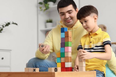 Baba ve küçük oğlu evdeki masada küplerle oynuyorlar.