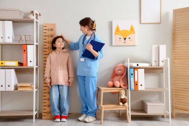 Klinikte stadyum ölçeri yakınında Asyalı bir kızın boyunu ölçen bir çocuk doktoru.