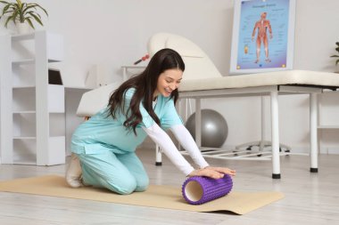 Rehabilitasyon merkezinde köpük silindirli kadın fizyoterapist.