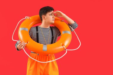 Kırmızı arka planda kurtarma halkası olan bir erkek denizci.