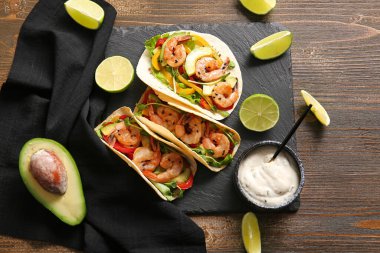 Lezzetli taze taco ve ahşap arka planda malzemelerle siyah tepsi.