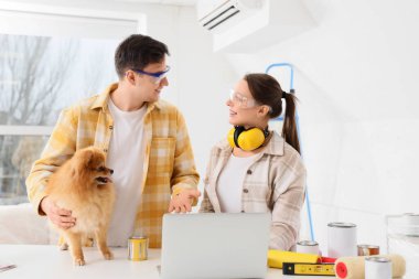 Pomeranya köpeği olan genç bir çift yeni evlerinin tamiri sırasında dizüstü bilgisayar kullanıyor.