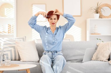 Olgun bir kadın evdeki kanepede kızıl saçlarını kesiyor.