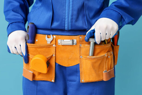 Механик с болтом в поясе инструмента на синем фоне, крупный план