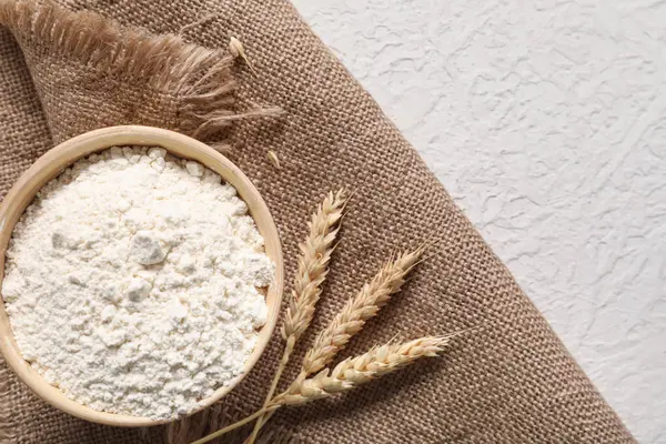 Açık arkaplanda bir kase buğday unu, dikenler ve çuval bezi.