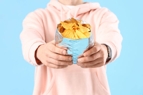 Man with tasty nachos on blue background, closeup