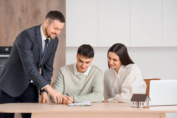 Real estate agent with couple signing house rental agreement at table in kitchen