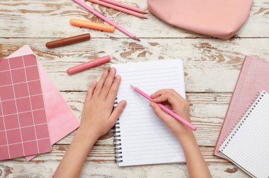 Çocuğun elleri kağıda beyaz ahşap arka plana bir şeyler yazıyor. Üst görünüm