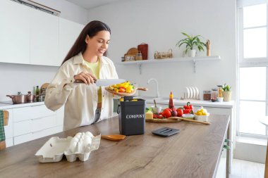 Mutfaktaki gübre için konteynıra yiyecek atan genç bir kadın.