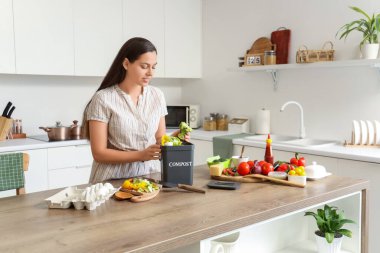 Mutfaktaki gübre için konteynıra yiyecek atan genç bir kadın.