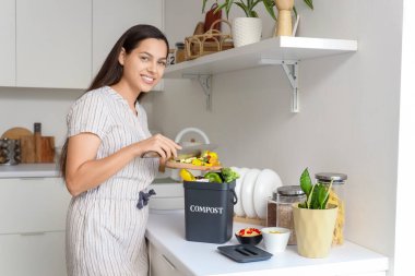 Mutfaktaki gübre için konteynıra yiyecek atan genç bir kadın.