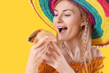 Şapkalı genç kadın sarı arka planda lezzetli taco yiyor, yakın plan.