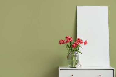 Yeşil duvarın yanındaki klozette laleli vazo ve boş poster.