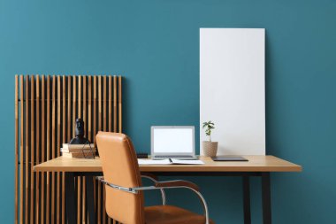Ofiste mavi duvarın yanında boş dizüstü bilgisayarı ve posteri olan bir işyeri.