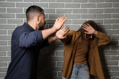 Genç adam gri tuğla duvarın yanında karısını dövüyor. Aile içi şiddet kavramı