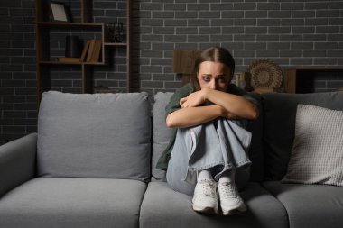 Evdeki kanepede oturan yaralı genç bir kadın. Aile içi şiddet kavramı