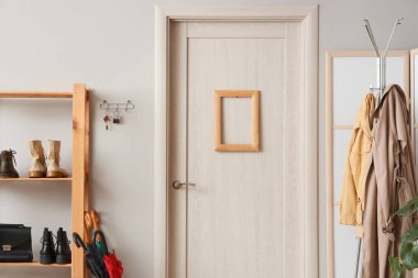 Elbise askısı, kapı, ayakkabı standı ve beyaz duvarda anahtar tutacağı olan şık bir salon.