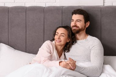 Yatak odasında battaniyenin altında el ele tutuşan mutlu çift