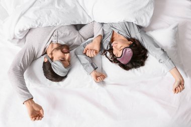 Uyku maskeli mutlu çift, battaniyenin altında yatıyorlar.