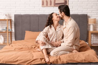 Pijamalı mutlu çift evde yatakta oturuyor.