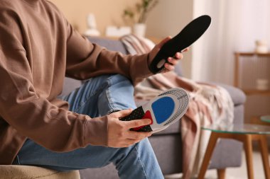 Genç adam evdeki ayağına ortopedik taban uyguluyor, yakın plan.