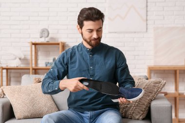 Ortopedik tabanı evdeki kanepede ayakkabıya takan yakışıklı adam.