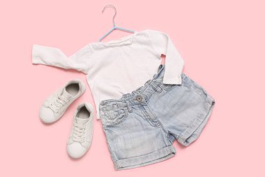 Şık çocuk kıyafetleri ve pembe arka planda ayakkabıları olan bir askı.