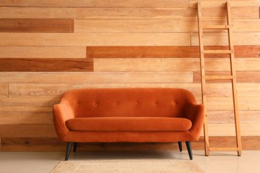 Oturma odasındaki tahta duvarın yanında merdiveni olan kırmızı kanepe.