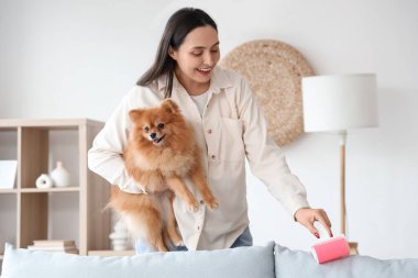 Evdeki kanepenin yanında tüylü köpeği ve pamuklu silindiri olan genç bir kadın.