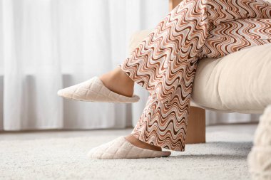 Evdeki yumuşak terliklerle kanepede oturan genç kadın.