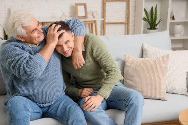 Olgun bir adam evdeki kanepede oğluna sarılıyor.