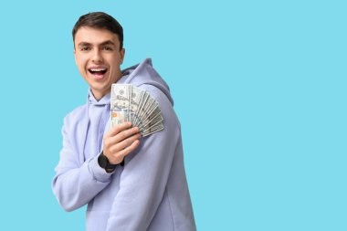 Mavi arka planda dolar banknotları olan mutlu genç adam.